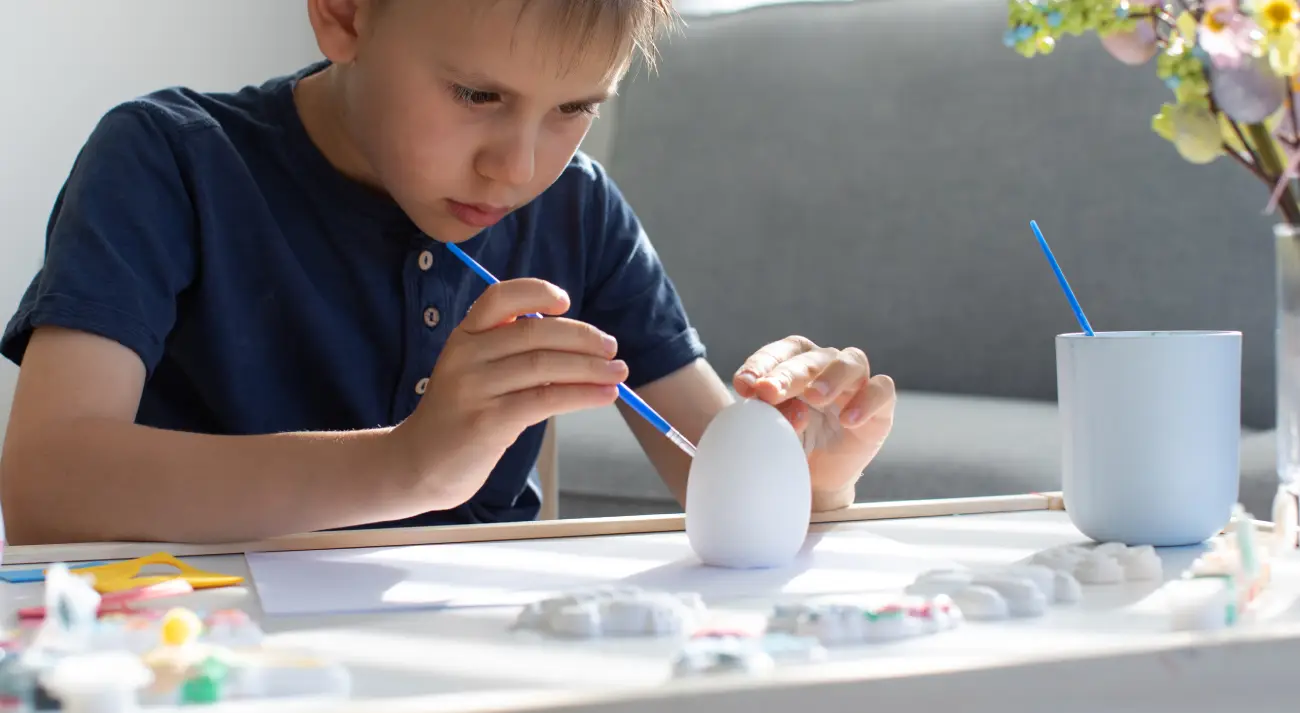 Child intensely focused on painting a plaster figurine, building cognitive skills and concentration at a table