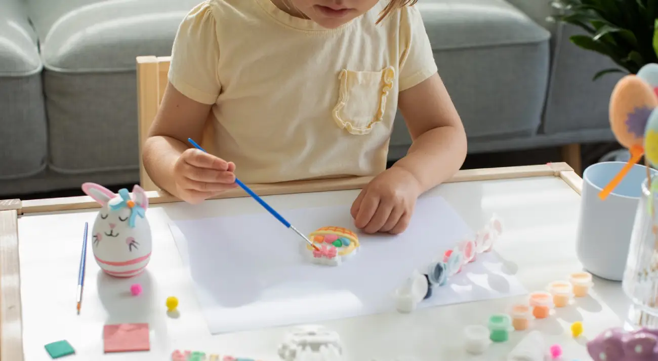 Young child painting a plaster craft kit with a fine brush at a table, improving hand-eye coordination and fine motor skills